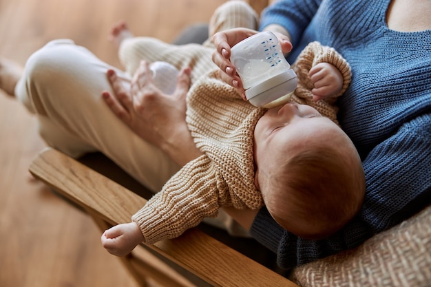 mother-feeding-her-newborn-baby-from-bottle-with-milk-woman-and-european-infant-kid-sitting-in...jpg