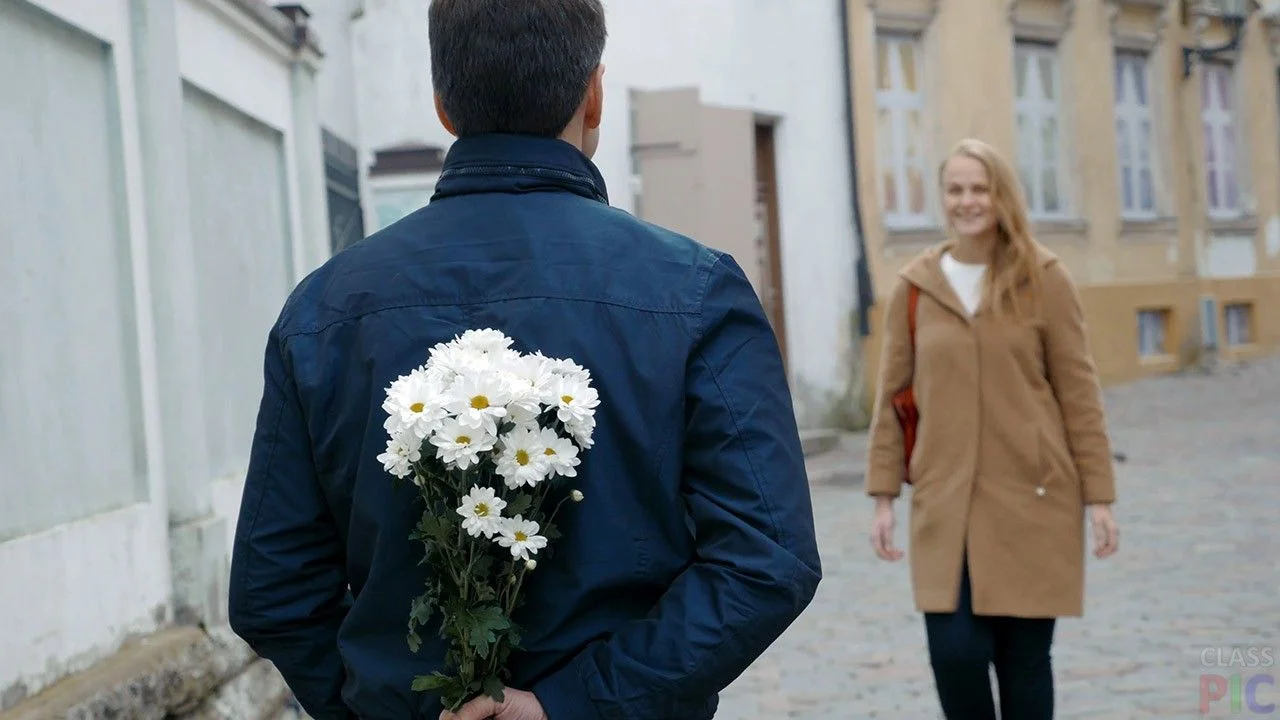 muzhchina-prjachet-za-spinoj-buket-belyh-hrizantem-devushka-idjot-k-nemu-navstrechu~2.webp