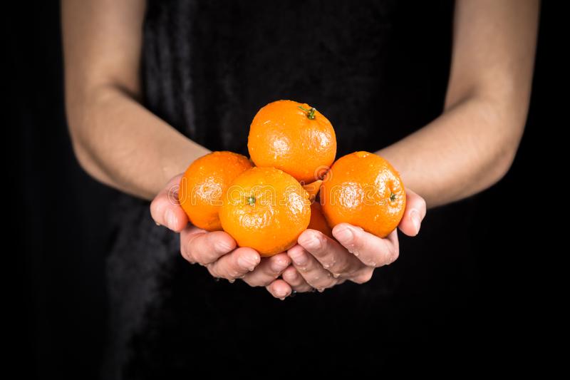 влажные-оранжевые-tangerines-в-руках-женщины-на-черной-предпосылке-136442407.jpg